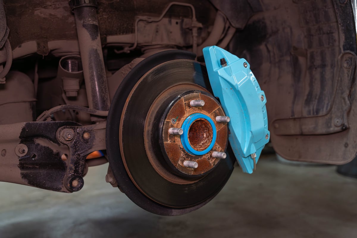 Mechanic working at an exposed wheel hub with the tire removed, servicing the brake rotor and caliper